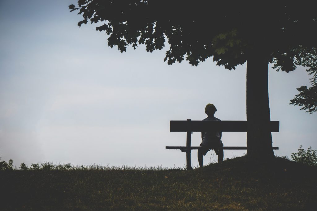 Person sitting alone on bench. Get therapy for depression to move your life forward today.