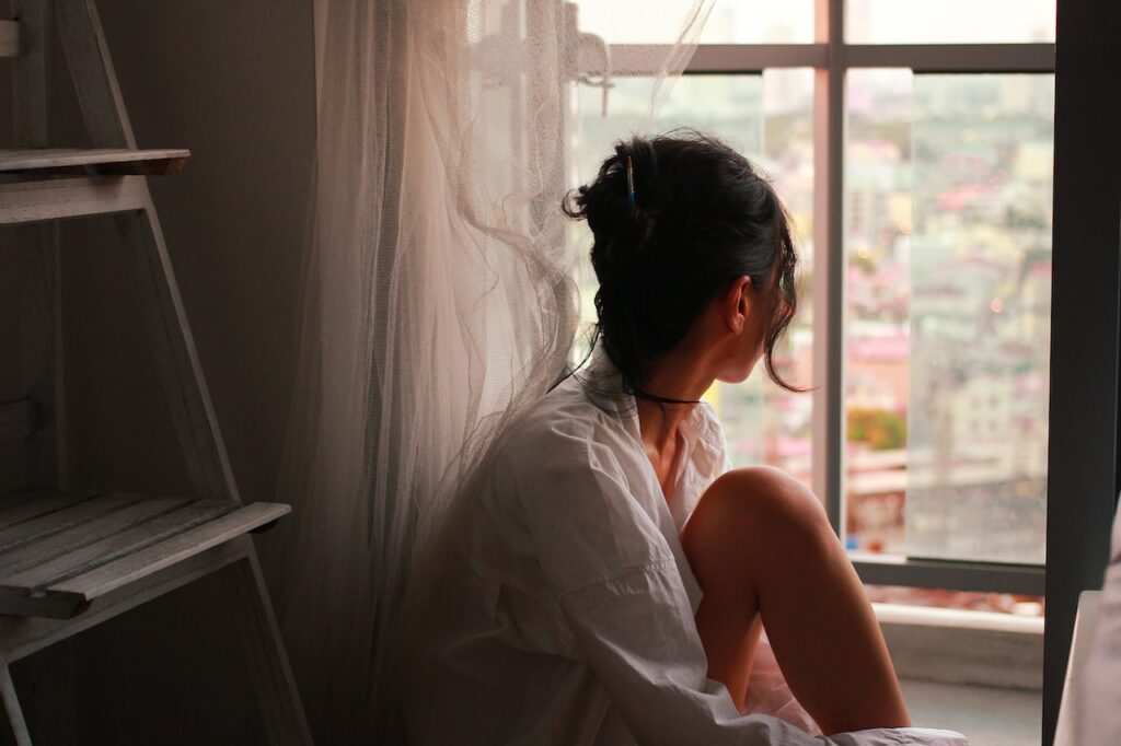 Woman looking out window, considering she might be depressed.