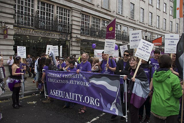 A group of asexual people marching with a banner, raising awareness for an asexual-friendly website and encouraging asexual-friendly therapy.